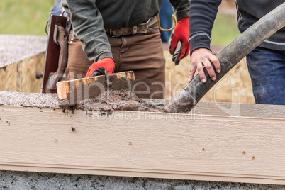 Construction Workers Pouring And Leveling Wet Cement Into Wood