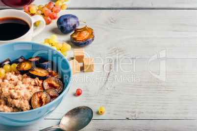 Porridge with fresh plum, green grapes and cup of coffee.