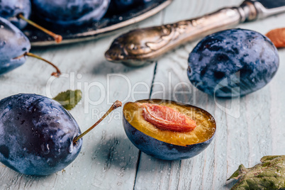 Plums with leaves and knife over wooden surface