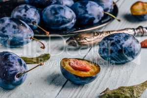Plums with leaves and knife over wooden surface