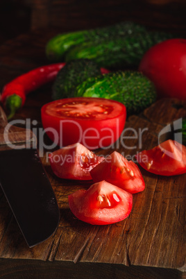 Sliced tomatoes on cutting board and cucumbers with chili pepper