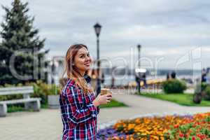 Beautiful young woman holding coffee cup and smiling in the park