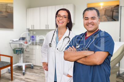 Hispanic Male and Caucasian Female Doctor Standing In Medical Office