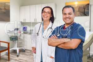 Hispanic Male and Caucasian Female Doctor Standing In Medical Office