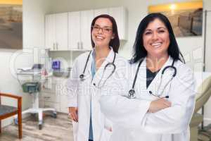 Hispanic and Caucasian Female Doctors Standing In Medical Office