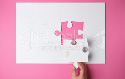 female hand puts white big puzzles on a pink background