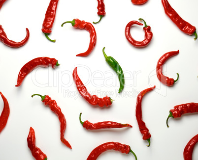 many red whole fruits of hot pepper and one green on a white bac