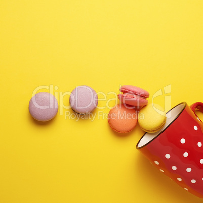 round multicolored macarons falling from a red ceramic cup with