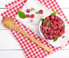 ripe red raspberries in a white wooden plate on a table