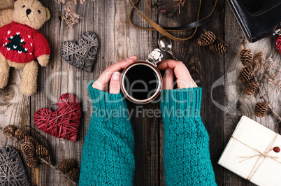 women's hands in a green knitted sweater holding a red ceramic m
