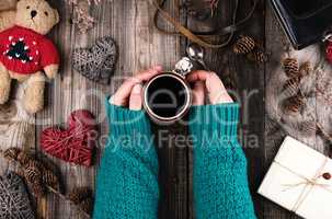 women's hands in a green knitted sweater holding a red ceramic m