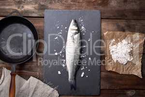 fresh whole sea bass fish on a black board