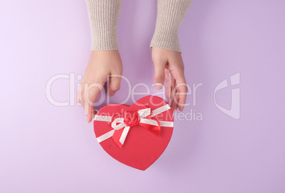 two hands hold a paper closed red box in the shape of a heart