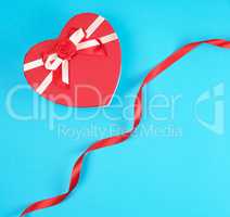 closed red heart-shaped gift box with a bow on a blue background