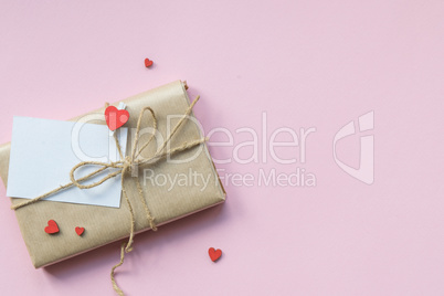 Present wrapped in brown craft paper and tie hemp string on Light pink background. Romantic Gift with decorative red hearts. Top view.