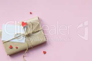Present wrapped in brown craft paper and tie hemp string on Light pink background. Romantic Gift with decorative red hearts. Top view.