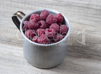 Ripe sweet raspberries in old rustic metal cup.
