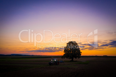 tractor with lights on at sunset