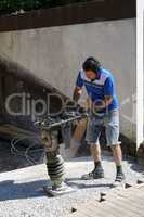 Construction worker compacting soil using compactor. Work with tamping machine