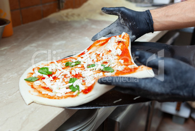 Raw margherita pizza on baking shovel.