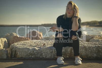 Blonde girl sitting on the rocks with cigarette in hand.