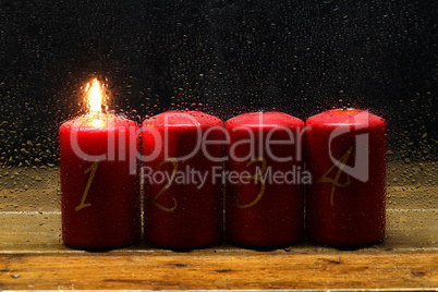 1 Advent. Advent candles in a row behind wet glass.