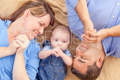 Young Mixed Race Couple Laying With Their Infant On A Blanket
