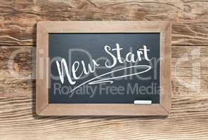 New Start Written on Slate Chalk Board Against Aged Wood Backgro