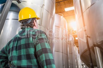 Man Wearing Hard Hat Looking Up At Large Industrial Tanks