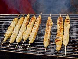 Meat dish wrapped in dough around wooden sticks is grilled