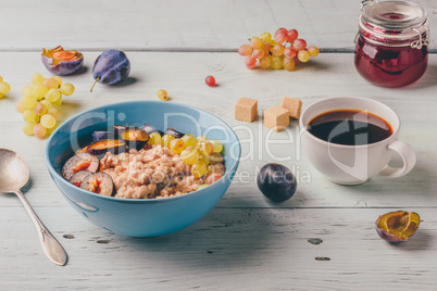Porridge with fresh plum, green grapes and cup of coffee.