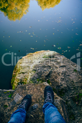 Men's legs stand on a stone in front of the lake.