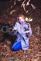 Porträt einer jungen Frau, die im Herbst auf dem Laub kniet und dies in die höhe wirft.