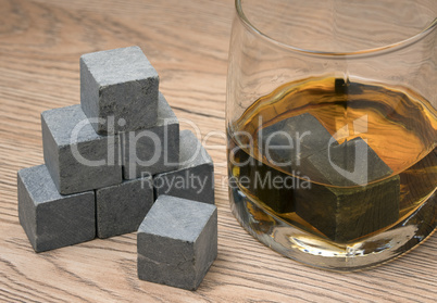 Stones in glass of whiskey on wooden background.
