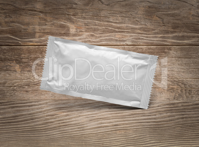 Blank White Condiment Packet Floating on Aged Wood Background