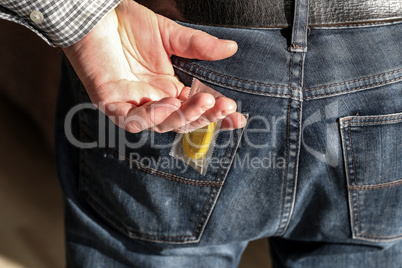 Hand takes condom packaging from jeans pocket