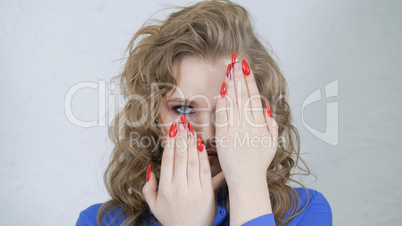 Girl is blonde with curly hair in a bright blue shirt. Hands with bright red nails on the face of a young girl.