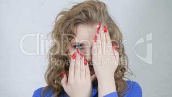 Girl is blonde with curly hair in a bright blue shirt. Hands with bright red nails on the face of a young girl.