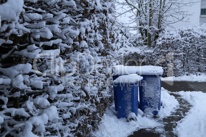 Blue dumpsters stand on a snow-covered street