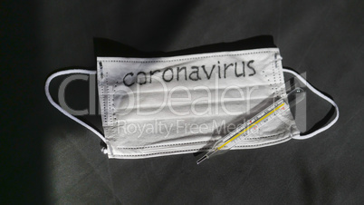 Coronavirus. Medical disposable gauze bandages are on the table. A mercury glass thermometer rests on a protective medical mask.