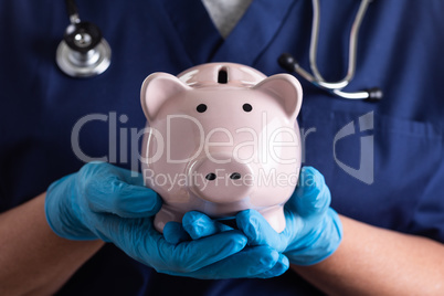 Doctor or Nurse Wearing Surgical Gloves Holding Piggy Bank
