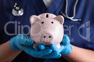 Doctor or Nurse Wearing Surgical Gloves Holding Piggy Bank