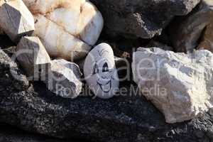 Funny face is drawn on a round pebble
