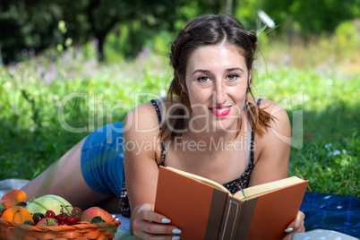 Girl with pigtails reads a book lying on the grass, during a pic