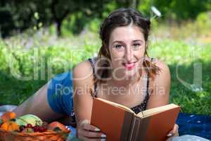 Girl with pigtails reads a book lying on the grass, during a pic