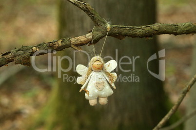 Figurine of a funny little angel hanging on a tree in the forest
