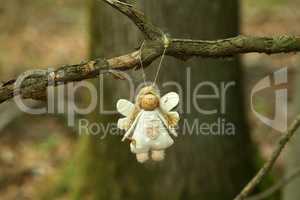 Figurine of a funny little angel hanging on a tree in the forest