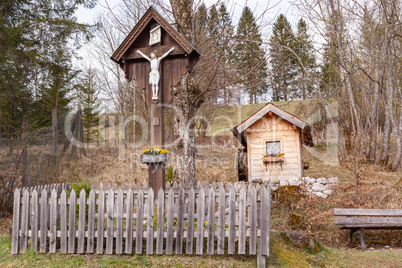 Wegkreuz mit Gartenhäuschen am Berg stehend