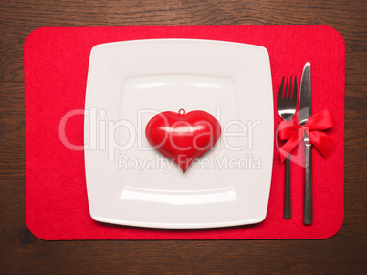 White plate with a red heart shape on wooden table