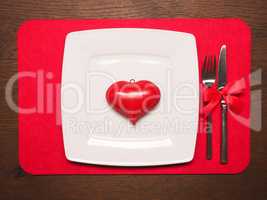 White plate with a red heart shape on wooden table